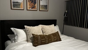 A neatly made bed with white linens and patterned pillows, a dark headboard, and three framed pictures on the wall above.