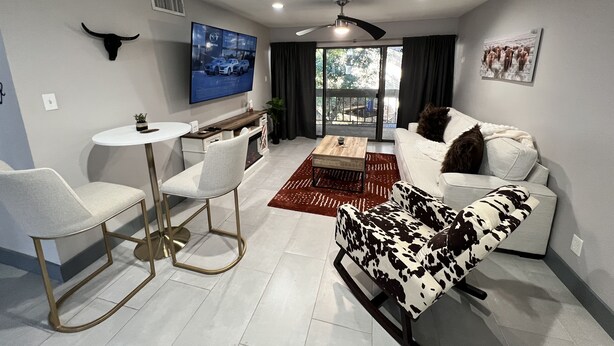 A modern living room with a white sofa, a patterned armchair, a coffee table, and a TV mounted on the wall.