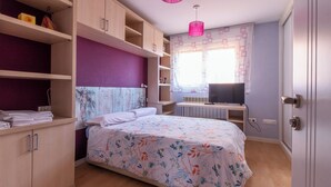 A bedroom with a bed, wooden cabinets, a TV, and a window with curtains.