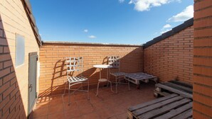 A small outdoor patio with a brick wall, a metal chair, a small round table, and a wooden bench.