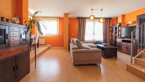 A living room with a sofa, a dining area with a table and chairs, a staircase, and a TV.