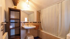 A bathroom with a white sink, a mirror, a shower curtain, a wooden shelf, and a small stool.