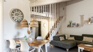 Ein modernes Wohnzimmer mit einem Holzes Esstisch, weißen Stühlen, einem grünen Sofa und einer Treppe.