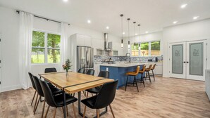 Una cocina moderna con una isla central, mesa de comedor de madera con sillas y vistas al exterior.