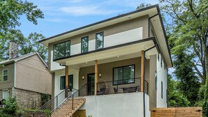 Una casa moderna de dos pisos con un porche cubierto, una escalera y un patio cercado.