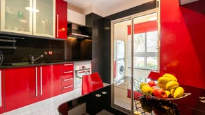Una cocina moderna con armarios rojos, una mesa de comedor con superficie de vidrio y un frutero.