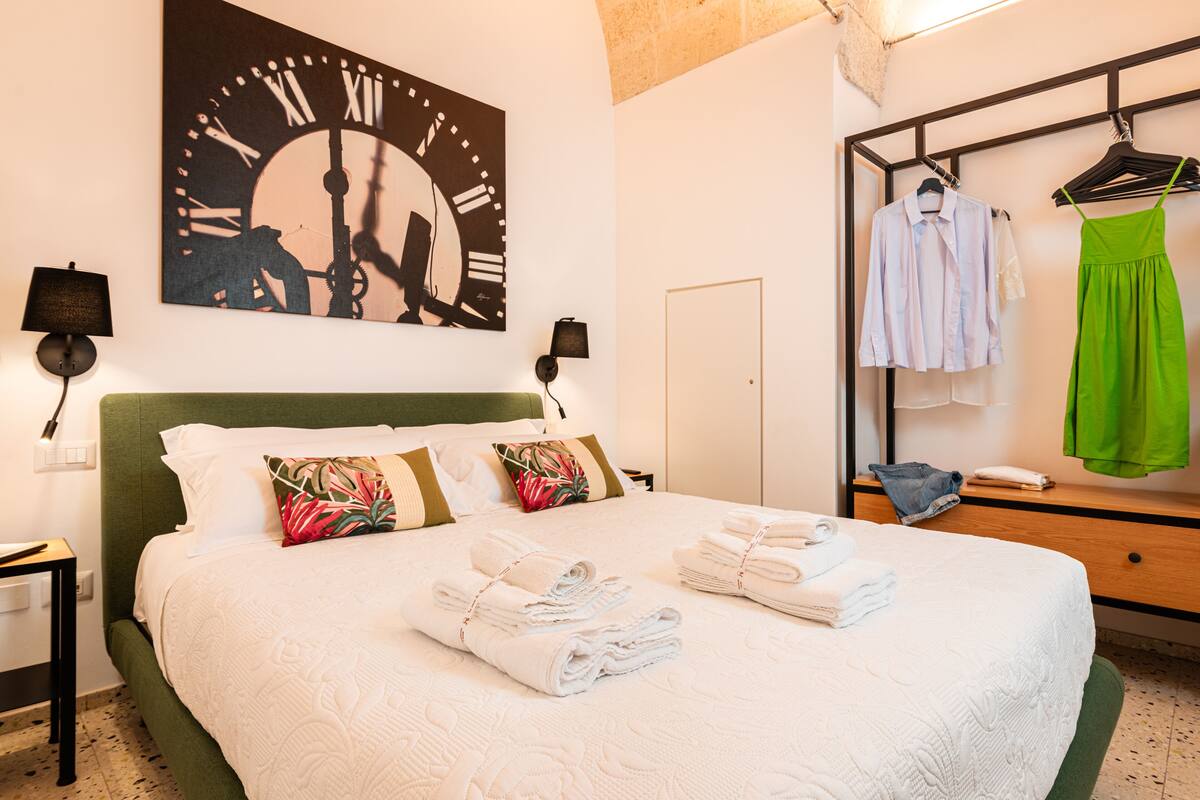 Una habitación de hotel con cama, un reloj en la pared, un armario y un espejo.