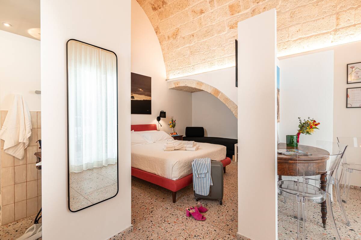 Una habitación de hotel con cama, escritorio, silla, espejo y baño.