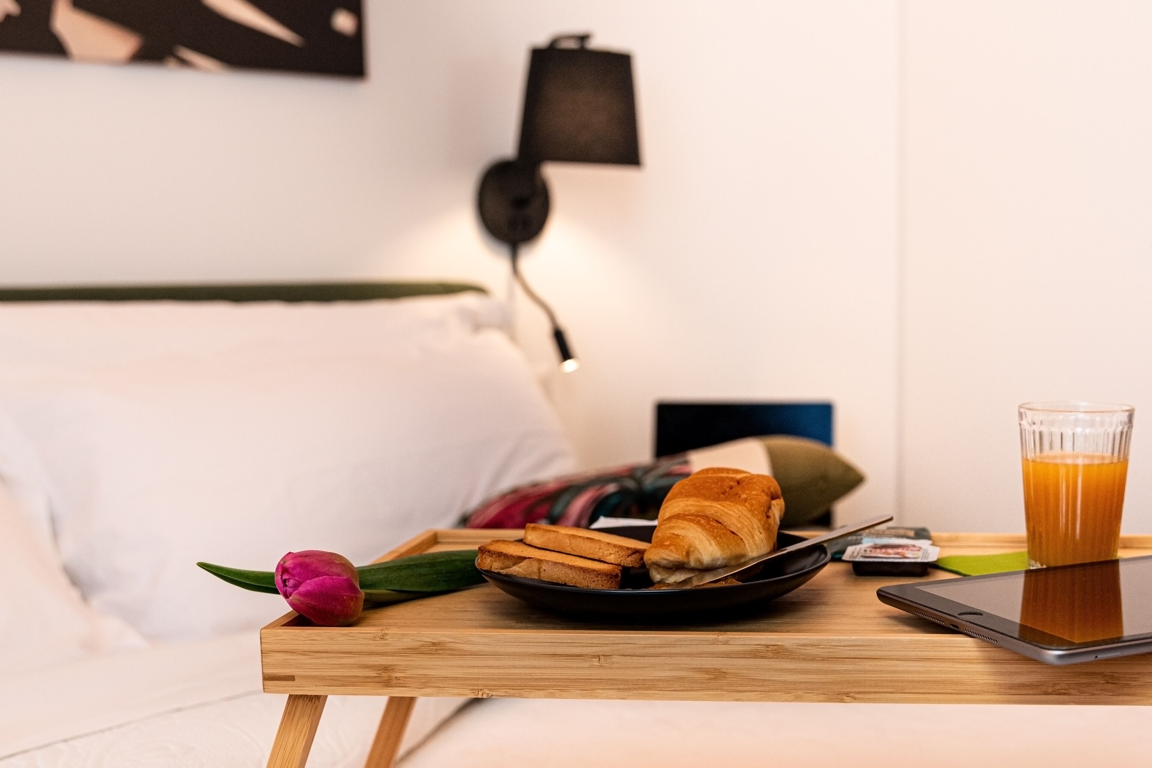 A breakfast tray with croissants, a glass of orange juice, and a smartphone on a wooden table in a hotel room.