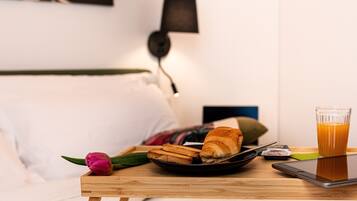 A breakfast tray with croissants, a glass of orange juice, and a smartphone on a wooden table in a hotel room.