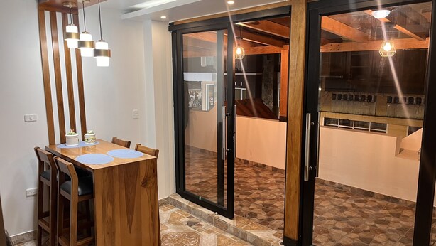 A dining area with a wooden table and chairs, a glass door leading to a balcony, and pendant lighting. - Kimsa Wasi (Otavalo)