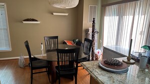 Zona pranzo con tavolo in vetro circondato da sedie, una lampada decorativa a soffitto e una finestra con persiane.