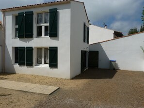 Un edificio de dos pisos con contraventanas verdes, una puerta visible y un pequeño espacio exterior con grava.
