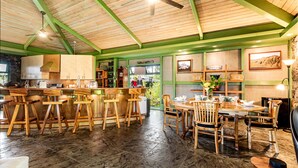Une cuisine spacieuse avec des tabourets de bar en bois, un coin repas avec une grande table et des chaises, et un ventilateur de plafond.