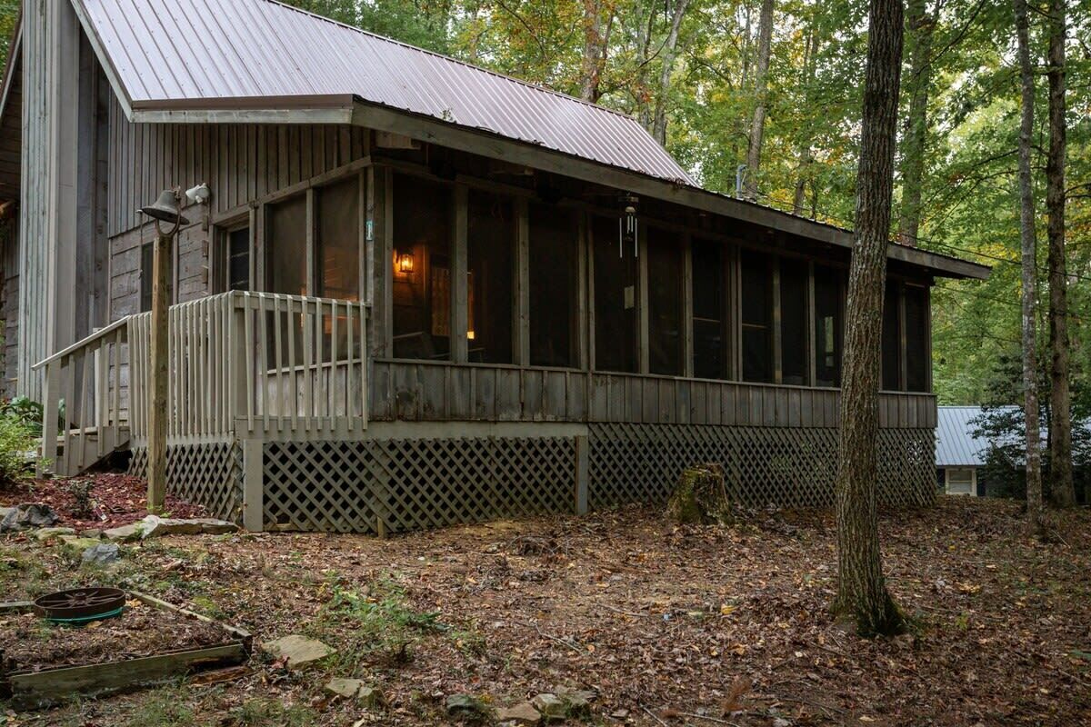 A rustic cabin with a porch, surrounded by trees.