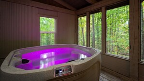 A hot tub in a wooden cabin with a window view of a forest. - Stylish Cabin Near Pigeon Forge (Sevierville)