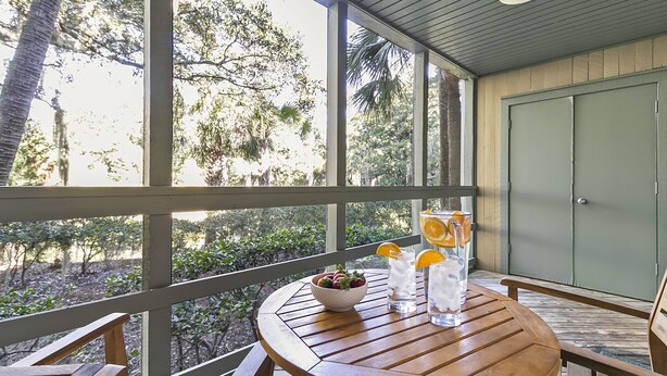 Une table en bois, sur laquelle se trouvent un saladier et des boissons, est placée sur un balcon d’où l’on peut admirer la vue sur les arbres.