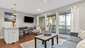 Un salon moderne comprenant un canapé, des fauteuils, une table basse, un téléviseur et une grande fenêtre avec des rideaux.