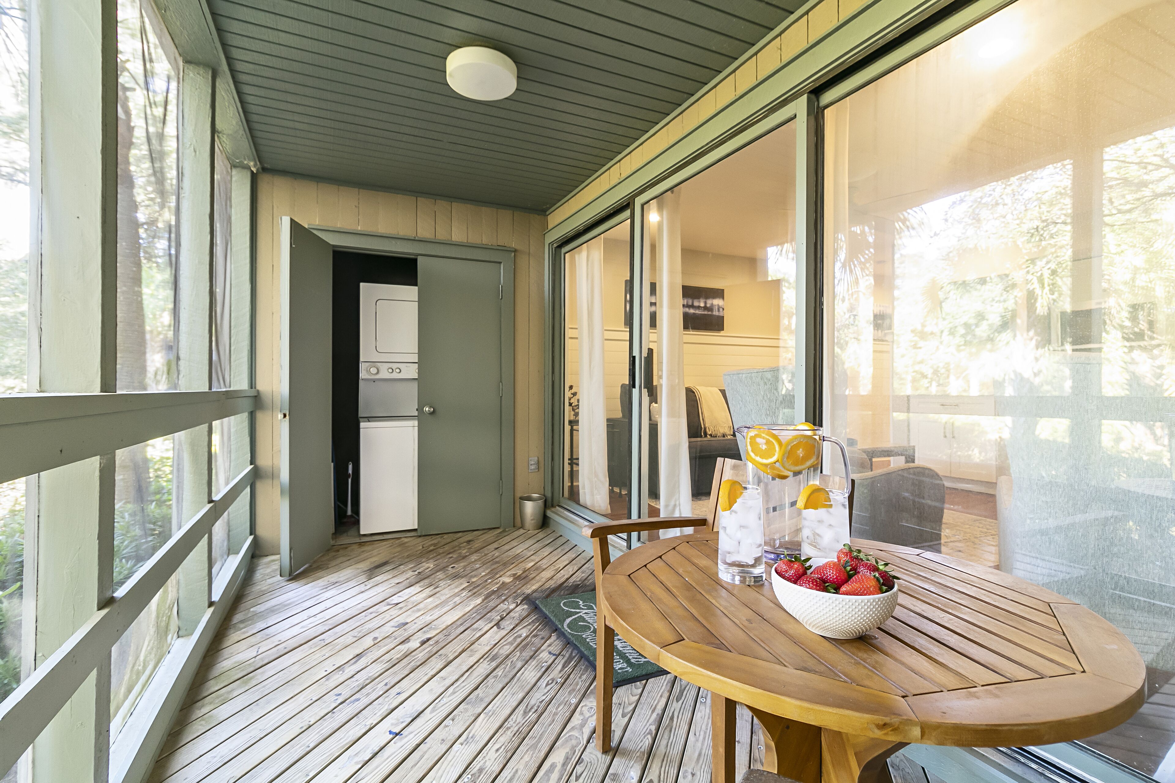 A wooden deck with a table and chairs, a bowl of strawberries, and a refrigerator in the background.