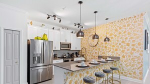 Et moderne køkken med rustfrie stålgrejs, en central ø med barstole, hængende lamper og et mønstret backsplash.