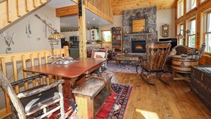 A spacious living room with a wooden staircase, a stone fireplace, and a large window. - Grandview Chalet - Modern & Luxurious Mountain Retreat with Panoramic Views (Grand Lake)