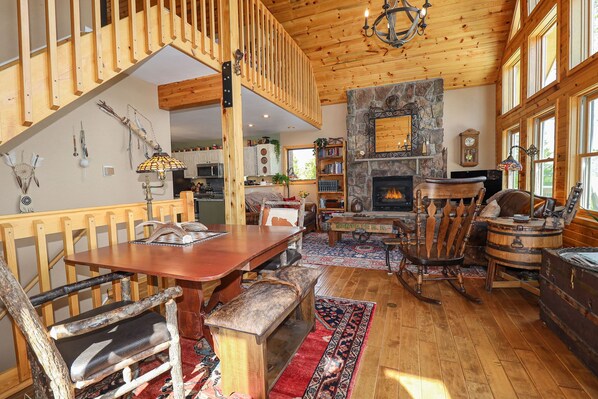 Un salón espacioso con una escalera de madera, una chimenea de piedra y un ventanal grande.