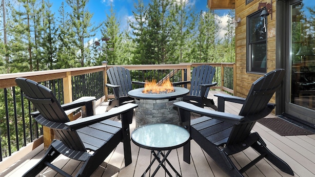 A deck with four Adirondack chairs, a round glass table, and a stone fire pit. - Grandview Chalet - Modern & Luxurious Mountain Retreat with Panoramic Views (Grand Lake)