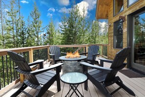 A deck with four Adirondack chairs, a round glass table, and a stone fire pit.