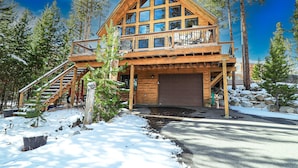 A two-story log cabin with a balcony, a garage, and a snow-covered driveway. - Grandview Chalet - Modern & Luxurious Mountain Retreat with Panoramic Views (Grand Lake)