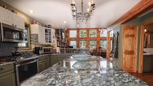 A spacious kitchen with granite countertops, a large island, and wooden cabinetry. - Grandview Chalet - Modern & Luxurious Mountain Retreat with Panoramic Views (Grand Lake)