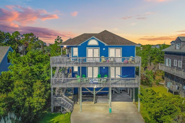 A two-story house with a balcony, surrounded by trees.