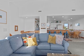 A living room with a blue sofa, a dining area with wooden chairs, and a kitchen in the background.