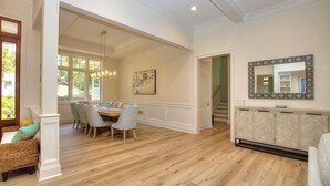 Un salón amplio con una mesa de comedor y sillas, un espejo grande y una escalera que lleva a otro nivel.