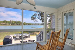 Une terrasse couverte avec vue sur un lac, des meubles d’extérieur et une chaise en bois.