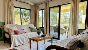 A room with a sofa, a coffee table, and a chair. There is a large window with curtains, and a view of the outdoors. - El Nido - Paradise In Cabo Pulmo! 2 Bedroom Villa by RedAwning (Cabo Pulmo)