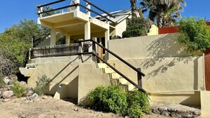 A two-story building with a balcony, a staircase, and a palm tree in the background. - El Nido - Paradise In Cabo Pulmo! 2 Bedroom Villa by RedAwning (Cabo Pulmo)