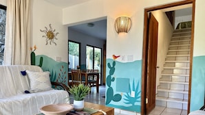 A living room with a sofa, a wooden table, a cactus wall mural, and a staircase. - El Nido - Paradise In Cabo Pulmo! 2 Bedroom Villa by RedAwning (Cabo Pulmo)