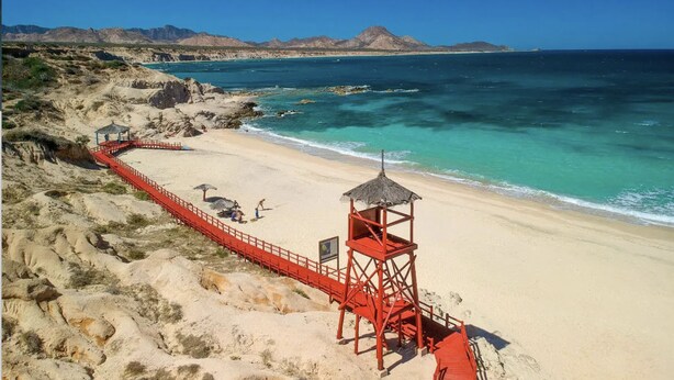 A beach with a red lifeguard tower and a red walkway leading to the water.
