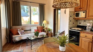 A cozy living room with a sofa, coffee table, and dining table, a kitchen with a stove and microwave, and a large window with curtains.