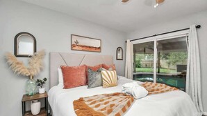 Een slaapkamer met een bed, nachtkastje, spiegel en een raam met uitzicht op een zwembad.