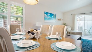A dining area with a wooden table set for four, surrounded by beige upholstered chairs. - SeaGlass: New Renovation Sleep 12 Hot tub, Pool (Sarasota)