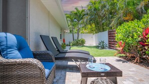 A patio with wicker furniture, a table with a glass, and a view of a garden with palm trees. - SeaGlass: New Renovation Sleep 12 Hot tub, Pool (Sarasota)