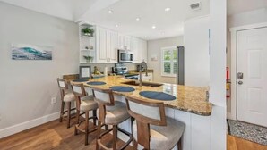 A modern kitchen with a central island, bar stools, and white cabinetry. - SeaGlass: New Renovation Sleep 12 Hot tub, Pool (Sarasota)