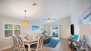 A spacious living room with a dining area, a large window with shutters, a ceiling fan, and a television. - SeaGlass: New Renovation Sleep 12 Hot tub, Pool (Sarasota)