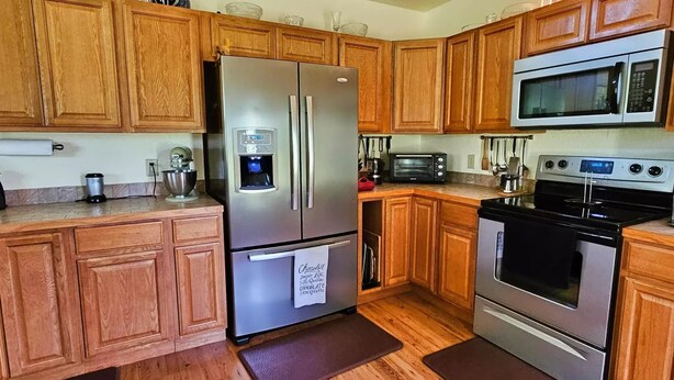 A kitchen with wooden cabinets, stainless steel appliances including a refrigerator, microwave, and oven, and a coffee maker. - The Haven of Peace in Madison County, FL (Lee)