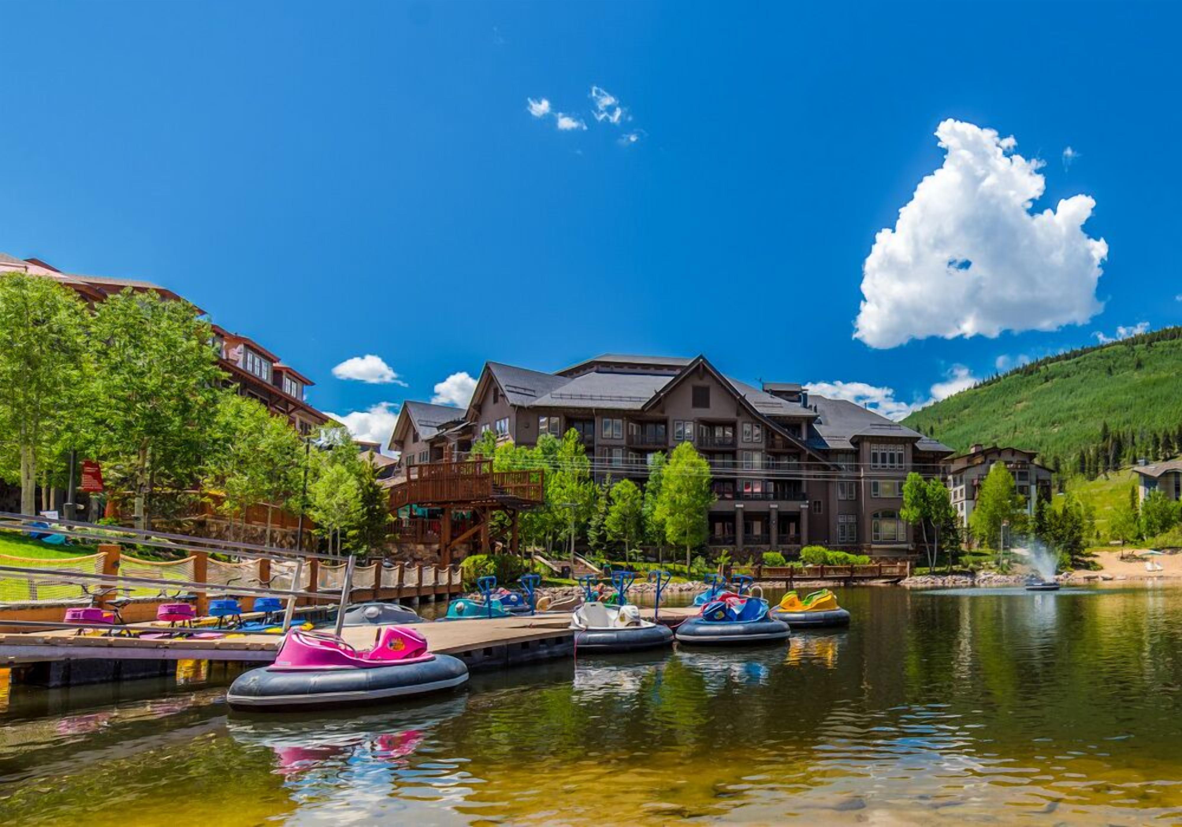 A lakeside hotel with a dock, paddle boats, and a large building with a sloped roof.