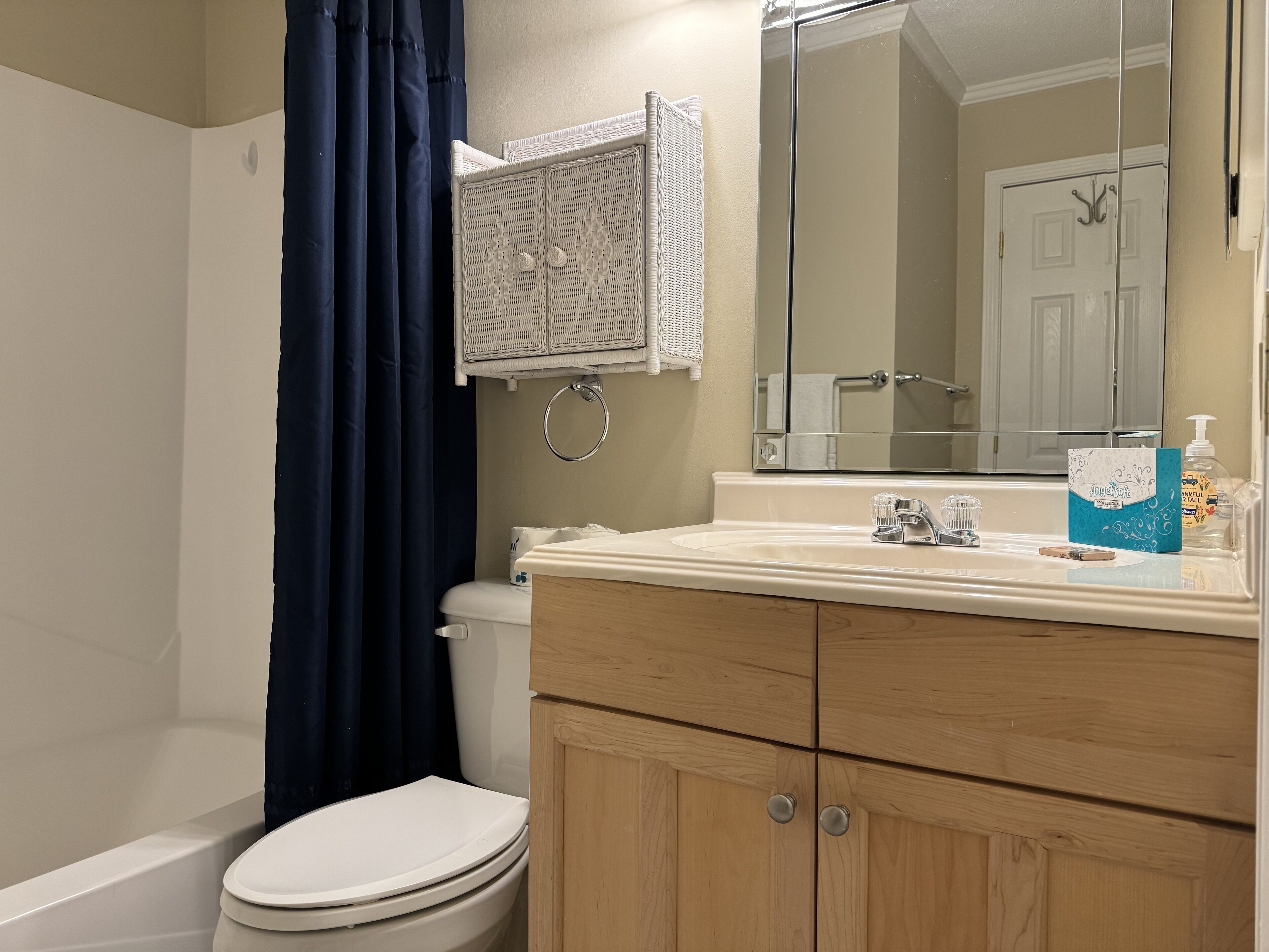 A bathroom with a white toilet, a wooden vanity with a mirror, and a blue shower curtain.