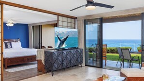 Ein Schlafzimmer mit großem Fernseher, einem Bett, einem Holzschrank und Blick auf das Meer.