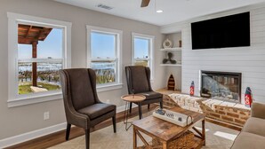 A living room with a fireplace, two armchairs, a coffee table, and a TV mounted on the wall. - Modern Waterfront Cottage on Wilmington by Lucky Savannah (Savannah)