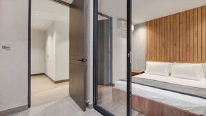 Un dormitorio moderno con cabecera de madera, cama con ropa blanca y puerta de cristal que da a otra habitación.